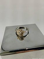 Front view of ring showing central diamond and surrounding diamond halo on metal display platform