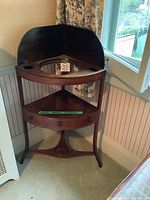 Full view of the antique mahogany corner wash stand placed in a room corner, showing the solid wood construction, single drawer with three knobs, and smooth curved legs.