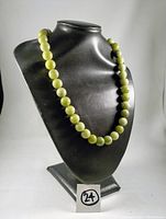 Full view of the jade bead necklace displayed on a black bust stand showing the full strand and bead uniformity.
