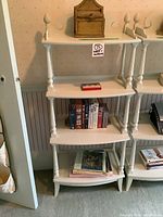 Full view of vintage 4 tier white painted wood bookshelf with carved column supports and various items on shelves.