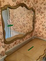 Front view of vintage mirror with ornate carved wood frame hung on floral wallpapered wall