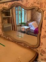 Front view of large vintage wall mirror mounted or placed on a piece of furniture, showing ornate scalloped frame with decorative molding at top center.