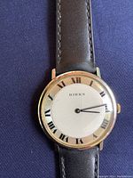 Close-up photo of the watch dial and leather strap on dark fabric background