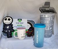 Photo showing all items in the lot including dog food container, Top Paw bowls and mat, Mud Buster paw cleaner, Halloween dog toys, and dog-themed coffee mug.