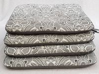 Stack of four gray and white floral patterned cushions showing thickness and ties.