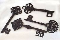 Four heavy decorative wrought iron keys arranged on a white background, showing the varied detailed bow designs and full length of keys.