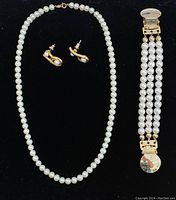 Full view of the imitation pearl necklace, pair of faux pearl and gold-colored stud earrings, and a faux pearl clothing cinch clip displayed on black surface.