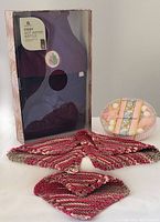 Boxed hot water bottle with cosy cover, decorative soaps in clear container, and three knitted dishcloths arranged in front.
