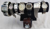 Overview of all eight watches on a black display stand showing various styles and band types.