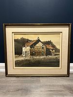 Framed watercolour painting of a rustic stone house with rusty roof in grassy field