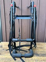Front view of folded black metal bike rack with straps on wooden surface