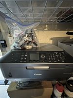 Canon all-in-one printer with control panel, LCD display, and 37 ink cartridges in a plastic bag on top.