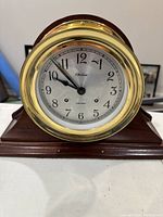 Front view of the Chelsea Shipstrike mantle clock showing white dial with black numerals and brass bezel on wooden body.