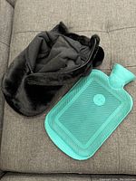 Black faux fur hot water bottle cover with attached pom-poms and green rubber water bottle