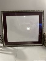 Full view of the custom ornate silver frame with maroon mat and glass; no artwork inside but some residue and dust visible inside glass.