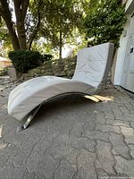 Side angle view of the custom grey leather reclining lounger showing its curved ergonomic design and chrome base, outdoors on paving stones.