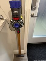 Assembled vacuum leaning against wall showing handheld unit, gold wand and direct drive floor head