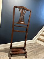 Front view of the wooden gentlemen's valet stand showing carved backrest, wristwatch rail, and base shelf.