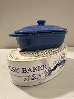 Blue ceramic goat cheese baker with lid placed on top of original cardboard box with decorative French text.