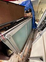 Four large frosted glass sliding door panels stacked with metal tracks visible, some dirt and storage marks seen.