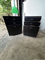 Two black Ikea filing cabinets side by side, one with drawers open, showing two small drawers above one large bottom drawer with file rails, set on small wheels.