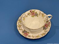Top view of floral bone china tea cup and matching saucer on a blue background showing pink and yellow flowers with gold trim