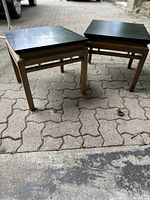 Pair of vintage mid-century side tables shown outdoors on brick-patterned surface from above and side angle.