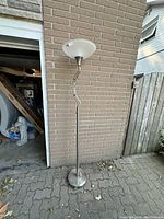 Full view of single tall up lamp with frosted glass shade and metal base on brick background