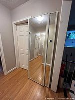 Photo showing two sliding mirrored closet doors installed with white wood grain look metal trim, set in an indoor hallway.