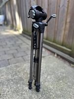 Folded Optex OPT255 tripod showing crank handle, locking knob, and compact design with carrying handle for easy transport.