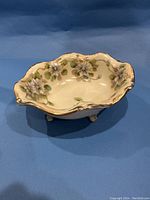 Oval vintage Nippon hand painted bowl shown from an angle to display shape, floral design, gold trim and feet.