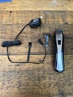 Top down image of the Wahl rechargeable clipper with power adapter, cleaning brush, and one interchangeable guide comb on a wooden surface.