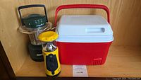 Green Rayovac lantern flashlight, yellow Hodgo lantern flashlight, and red/white Rubbermaid cooler