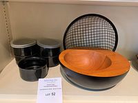 Photo of solid wood bowl with black base, black metal mesh bowl, and five small black containers with two lids.