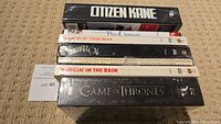 Stack of six DVD cases including Citizen Kane, White Christmas, Doctor Zhivago, Wizard of Oz, Singin' in the Rain, and one Game of Thrones box at the bottom. All sealed in plastic wrapping.