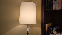 Full view of chrome floor lamp with white drum shade, turned on