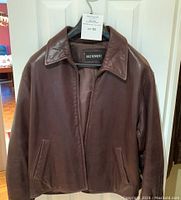 Front view of brown leather bomber jacket hanging on door