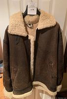 Full front view of jacket hanging open showing exterior leather and shearling lining