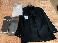 Full view of tuxedo jacket, trousers, shirt and boxed accessories laid out on bedspread