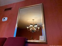 Front view of the large rectangular mirror hung on a red wall reflecting a chandelier.