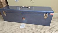 Closed rectangular blue metal tool box with two clasps, silver handle, and Beach Brand logo on front.