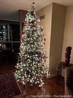 8-foot pre-lit Christmas tree decorated in a living room with integrated white lights turned on. Decorations are visible but not included in lot.