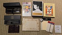 Overview of the lot showing pens in boxes, notecards with artistic covers, stationery accessories like card holder and tabs, and a roll of postage stamps.