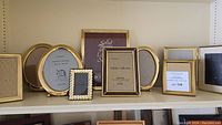 Shelf display of multiple vintage solid brass photo frames in various sizes and styles.