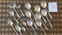 Full overhead view of all 15 sterling silver spoons and ladles arranged on patterned cloth