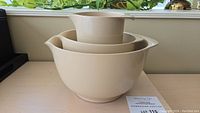 Side view of three beige nesting Rosti bowls stacked inside each other showing the spout and handle design