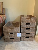 Eight wicker baskets arranged in two stacks—three larger on left, five smaller on right—showing cut-out handles and uniform weave.