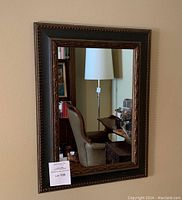 Full view of the rectangular wood framed mirror hung on a beige wall reflecting a room with furniture.