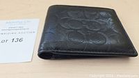 Side view of black leather Coach wallet showing embossed pattern and folded shape.