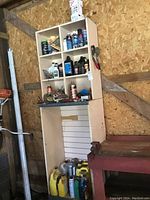 Photo showing shelving with various automotive fluid containers in different sizes and colors including yellow jugs and aerosol cans on a wooden shelf.